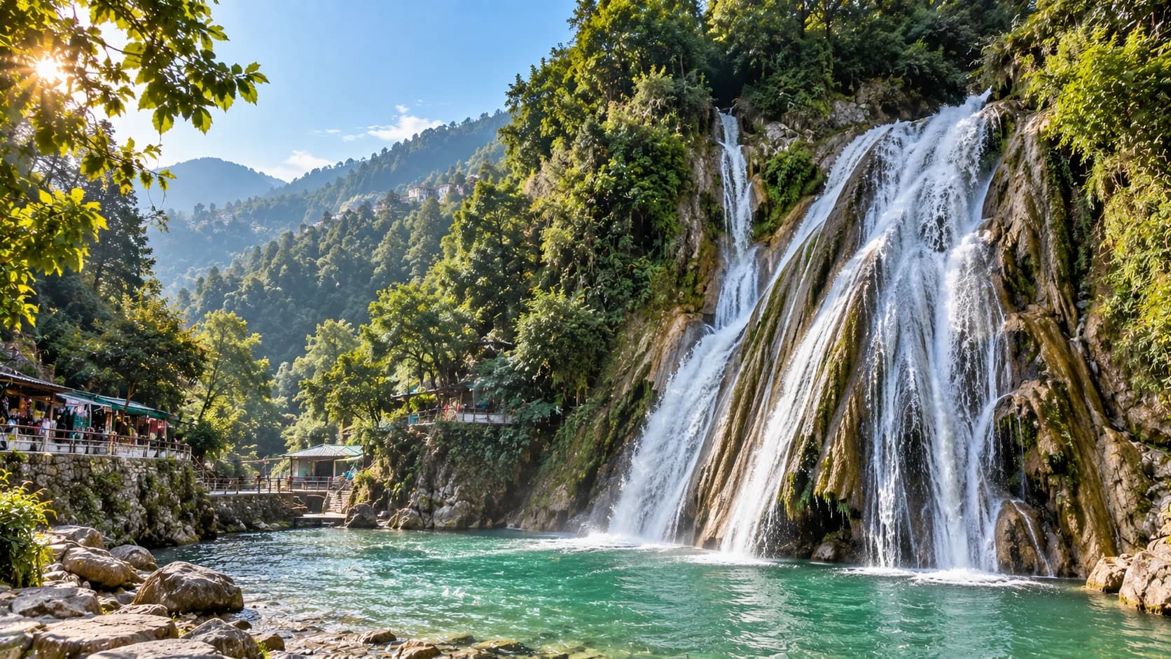 A waterfall dropping in several strands into a green pool near Mussoorie, with viewing platforms and forested hillside alongside